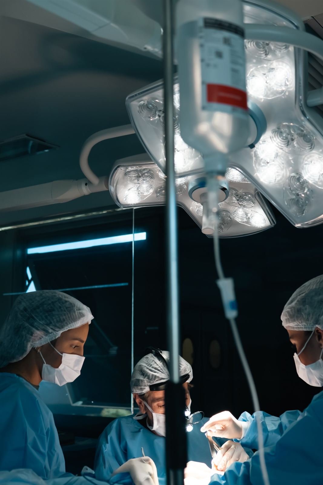 Equipe cirúrgica operando sob o foco, com soro em primeiro plano